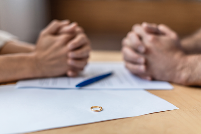 Couple with hands clasped across a table with a wedding ring on documents symbolizing shallow man&rsquo;s relationship issues.