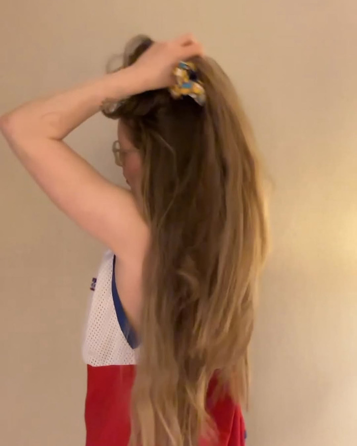 Harry Potter star with long hair, wearing glasses and a red and white top, adjusting her hair indoors.