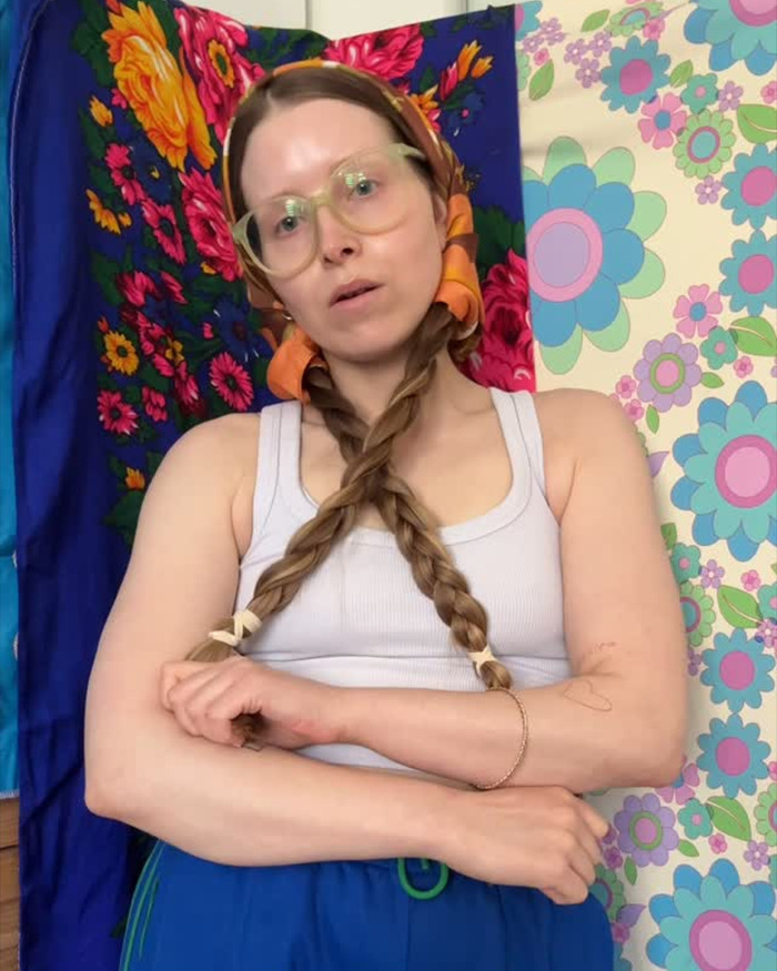 Harry Potter star with braided hair and glasses in casual wear against a vibrant floral and patterned background.