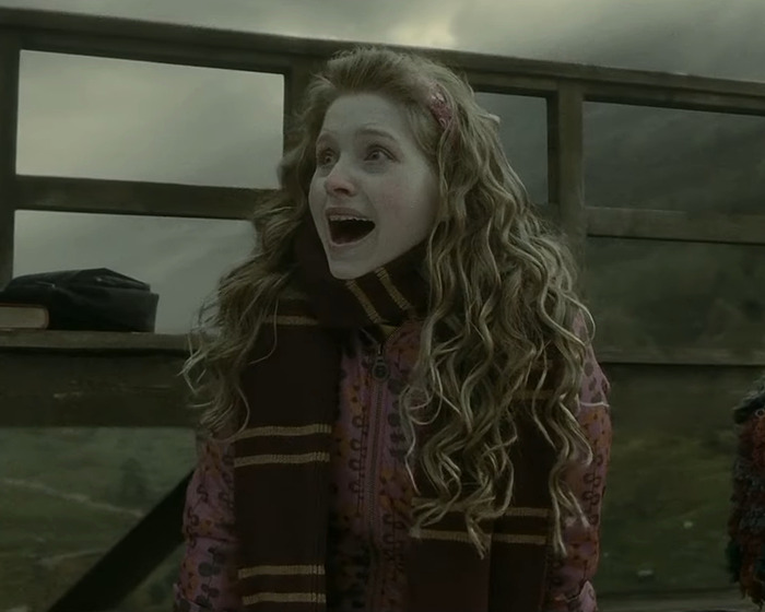 Harry Potter star with curly hair wearing a scarf reacts emotionally in an outdoor fan event scene.