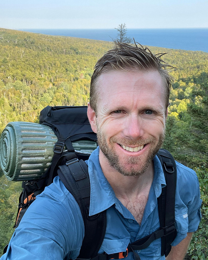 Smiling hiker with backpack and rolled sleeping mat in a forested mountain area, representing hiker’s tragic last text. Smiling hiker with backpack and rolled sleeping mat in a forested mountain area, representing hiker’s tragic last text.