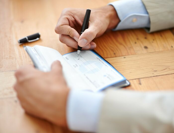 Man writing a check on a wooden table showing everyday things that humble fully grown adults in daily life.