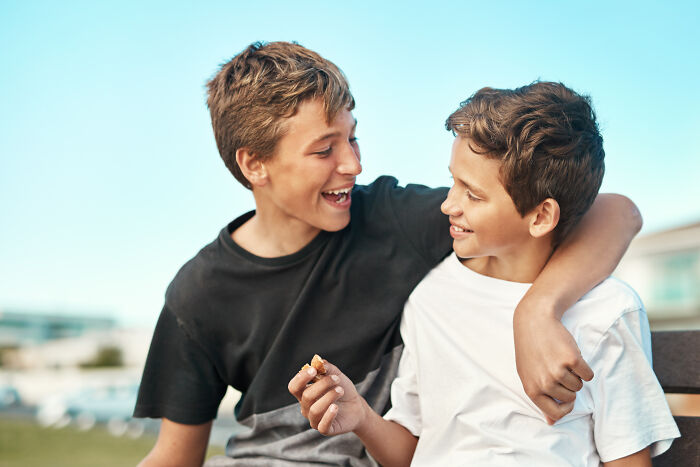 Two boys laughing and sharing a snack outdoors, showing the unexpected moments sewer workers sometimes experience.