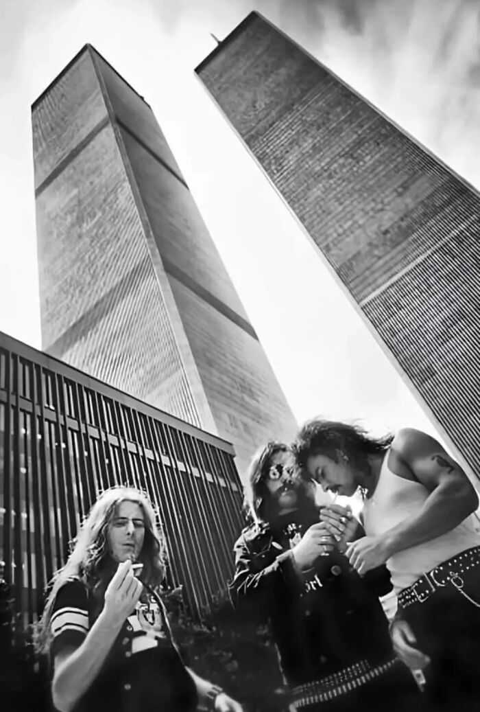 Black and white photo of three men smoking with towering skyscrapers behind, illustrating perception of time and comparisons.