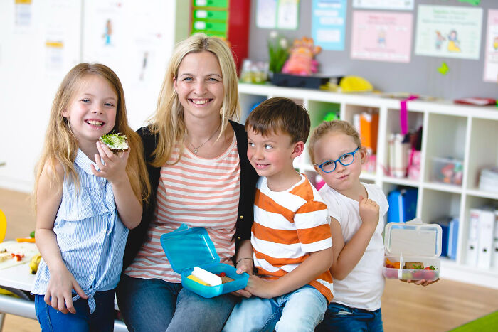 Happy woman with three kids smiling in a colorful classroom, illustrating challenges of the worst partner ever concept.