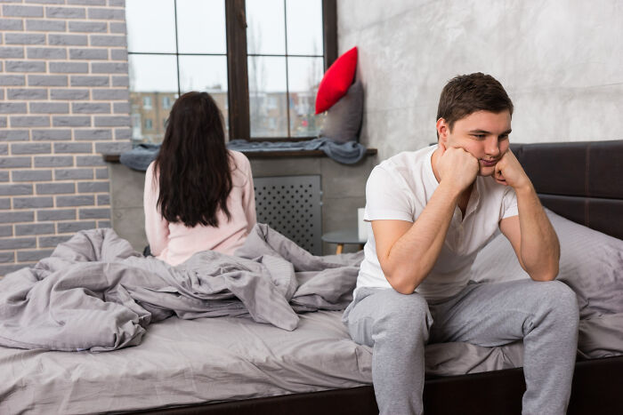 Couple sitting apart on bed looking upset, illustrating signs of the worst partner in a troubled relationship.