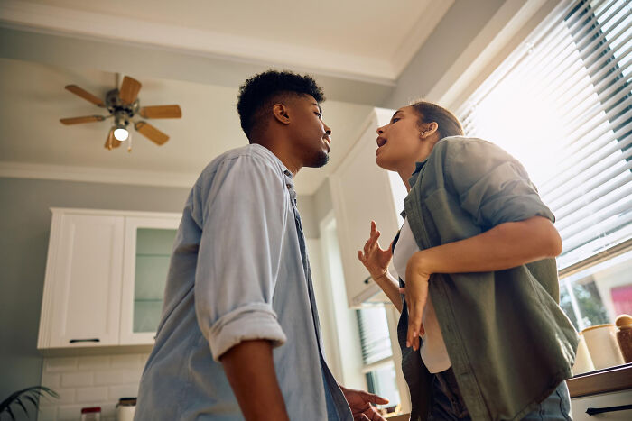 Couple arguing intensely in kitchen near window, showing signs of the worst partner ever in a tense relationship moment.