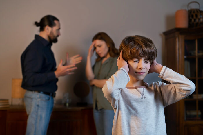 Child covering ears upset while parents argue in background, illustrating signs of the worst partner ever behavior.