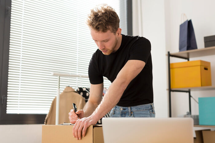 Young man packing a box in a bright room, illustrating signs of the worst partner ever in a relationship.