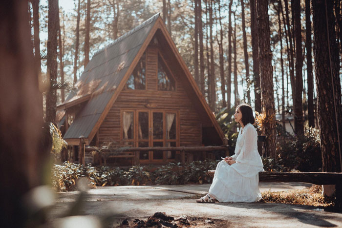 Bride in a white dress sitting alone outdoors near a wooden cabin, showing a bridezilla moment during a wedding photoshoot crash.