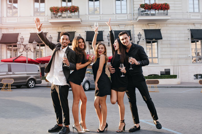 Group of young people celebrating outdoors, raising glasses, capturing the chaos of strangers crashing a wedding photoshoot.