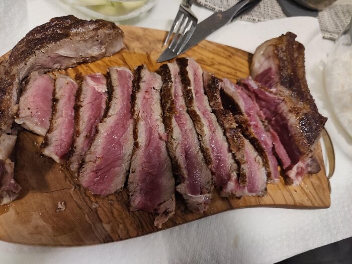 Person cutting a rare steak with roasted tomatoes and potatoes on a plate, an everyday thing humbling adults.