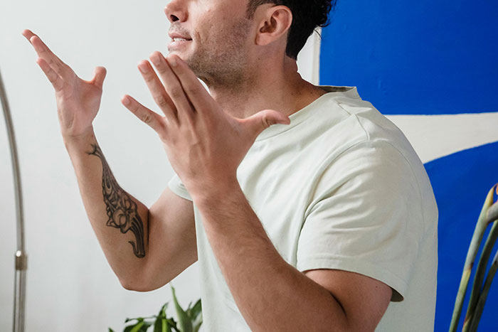 Man with tattoo on arm expressing frustration indoors near plants and blue wall, illustrating conflict in family relationships.