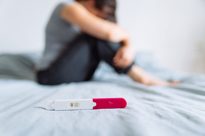 Pregnancy test on bed focus with a blurred person sitting in the background, highlighting secret digging through trash situation.