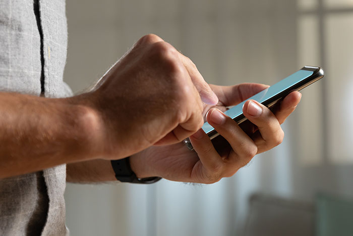 Close-up of a man using a smartphone to message, illustrating husband posing as pregnant wife for loyalty test.
