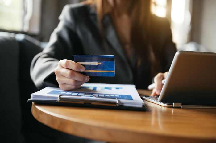 Woman holding credit card and using laptop, concerned about huge debt and financial secrets in a home setting.
