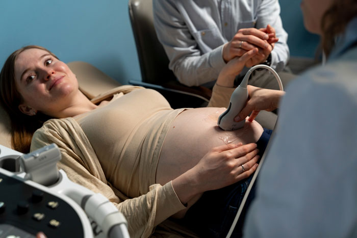 Pregnant woman undergoing ultrasound during IVF treatment, while husband looks anxious holding her hand in a clinic setting.