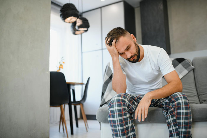 Man sitting on a couch looking anxious and distressed during wife's IVF treatment, reflecting husband anxiety after marriage.