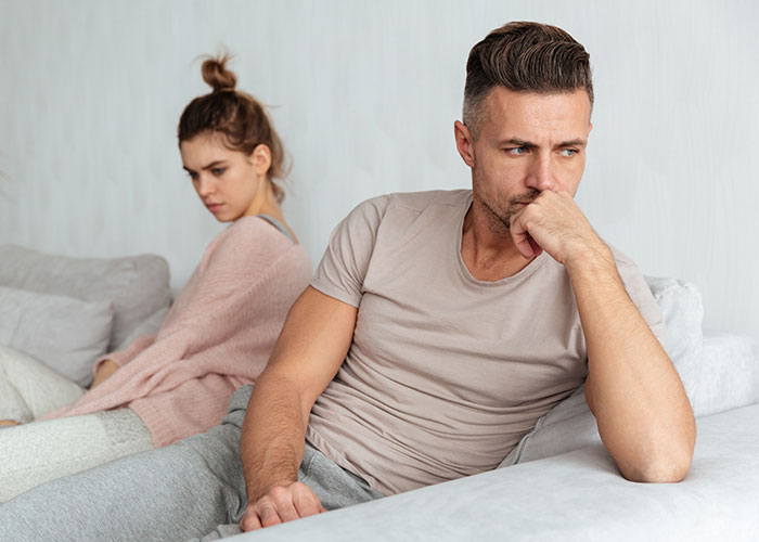 Husband and wife sitting apart on couch looking upset, reflecting tension in intimacy boundaries and relationship issues.