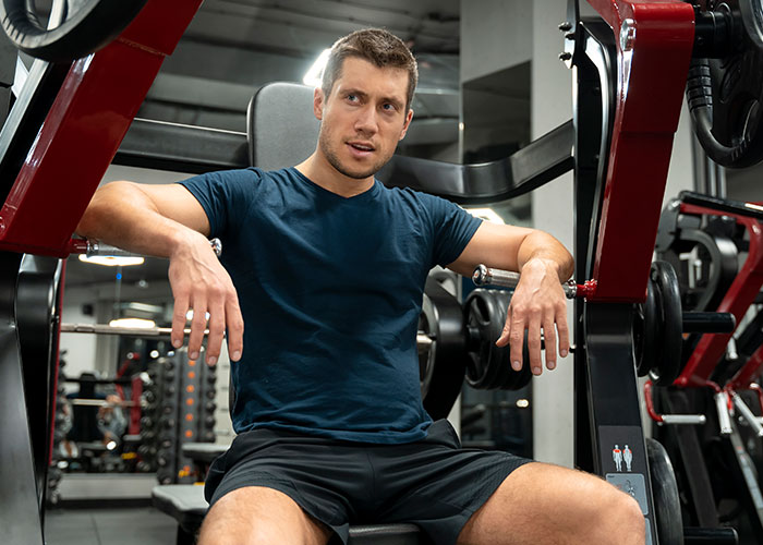 Man in a gym resting on exercise equipment, appearing thoughtful about intimacy boundaries and relationship issues.