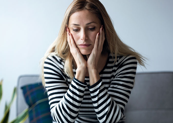 Worried woman sitting with hands on her face, reflecting on intimacy boundaries and relationship concerns at home.