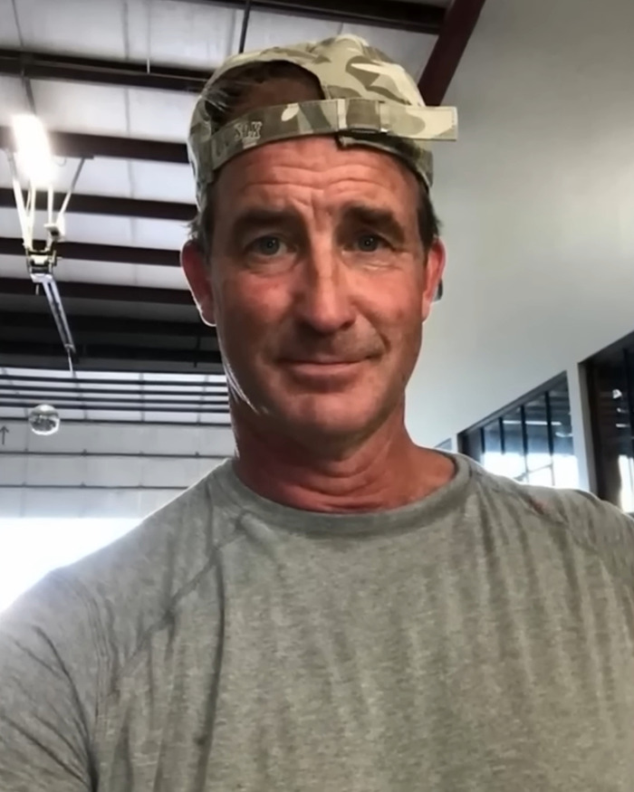 Man in a camo cap and gray shirt in a warehouse setting related to Coldplay KissCam saga unexpected twist.