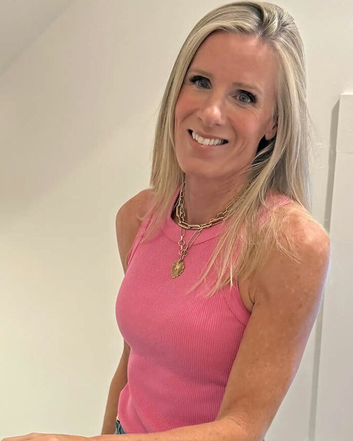 Smiling woman in a pink sleeveless top and gold necklaces posing indoors related to Coldplay KissCam saga news.