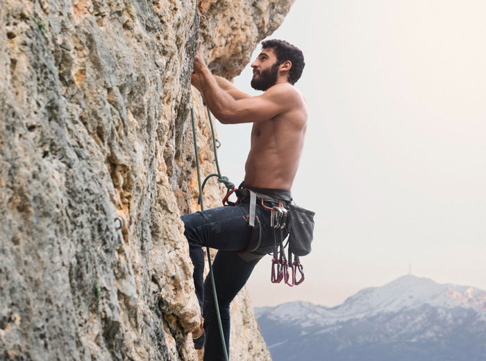 Man rock climbing shirtless outdoors, illustrating husband spending nearly 12K yearly on his hobby.