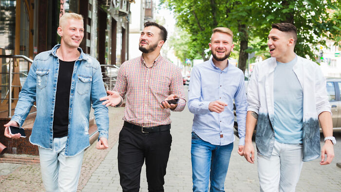 Four men walking outdoors, smiling and talking, illustrating reasons women might get the ick from a guy.