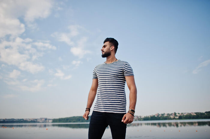 Man standing outdoors by a lake wearing striped shirt, representing reasons women got the ick from a guy concept.