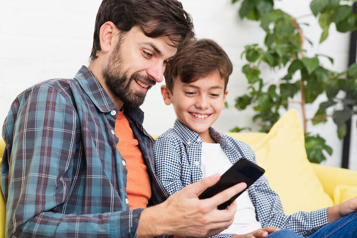 Man and boy smiling while looking at a phone, illustrating reasons why women get the ick from a guy.