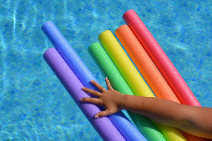 Hand reaching for colorful pool noodles floating in clear blue water illustrating reasons women got the ick from a guy.