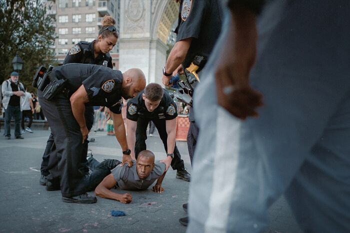 Police officers detaining a man on the street, captured in a striking street photo that feels like a movie still.