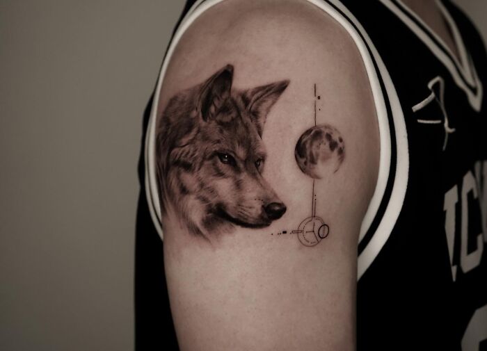 Realistic dog tattoo on upper arm with moon and geometric elements by Korean tattoo artist specializing emotional pet tattoos.