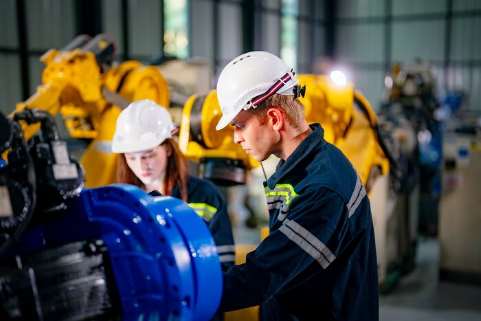 Two engineers wearing helmets working on industrial machinery, highlighting out of touch workplace situations.