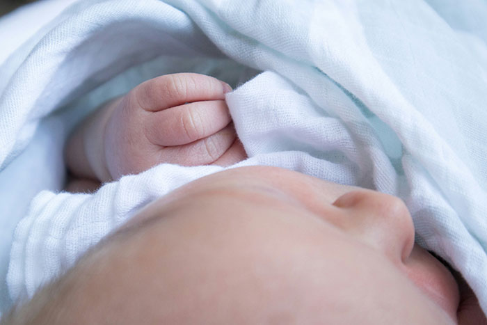 Newborn baby wrapped in white blanket, related to autopsy findings revealing gender in a cheerleader's closet case.