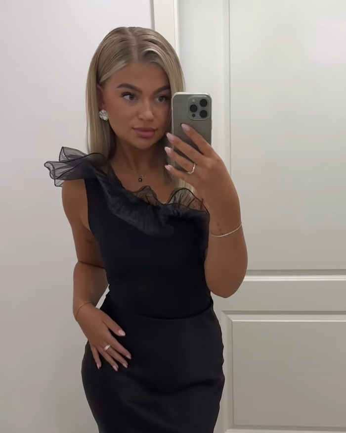 Woman wearing a black dress taking a mirror selfie, showcasing her engagement ring in a viral engagement post reaction. Woman wearing a black dress taking a mirror selfie, showcasing her engagement ring in a viral engagement post reaction.