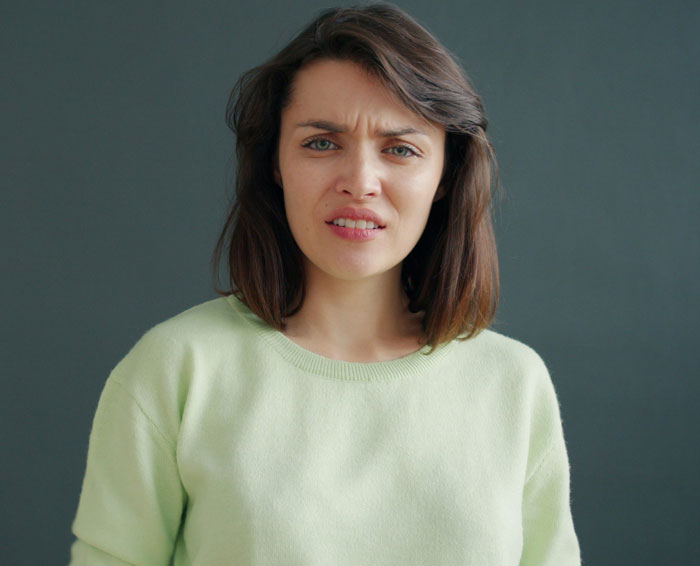 Woman in light green sweater with a concerned expression, illustrating red flags in a relationship about earning differences.
