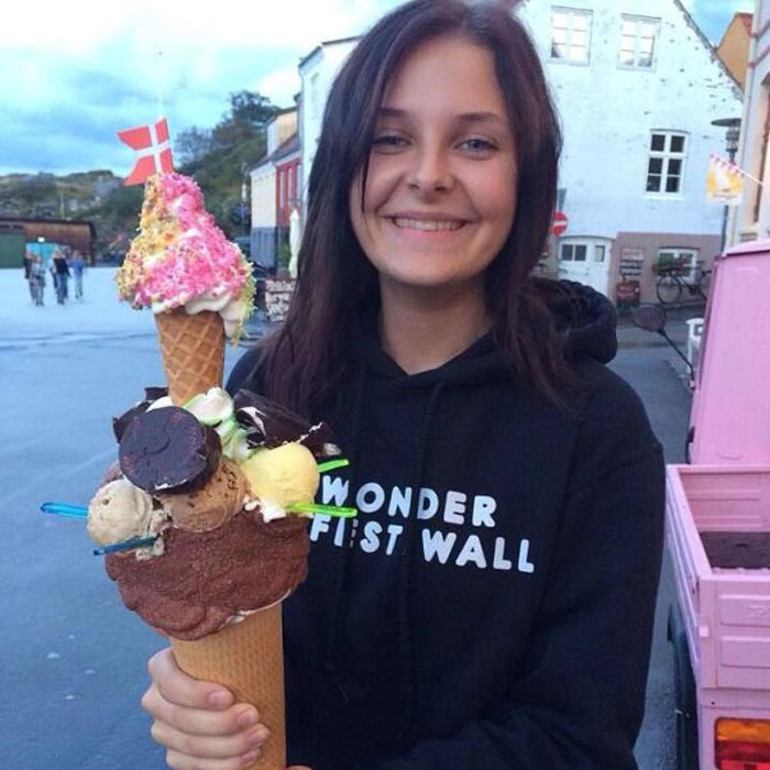 Smiling young woman holding large colorful ice cream cone with Danish flags on a street in Denmark.
