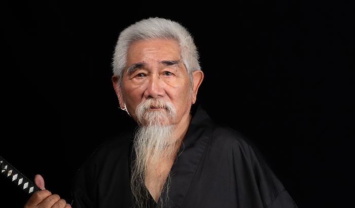 Elderly man with long white beard holding a katana, representing useless yet fascinating knowledge concept.