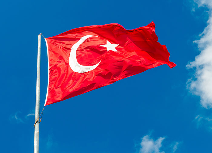 Red Turkish flag waving on a flagpole against a clear blue sky, representing fascinating knowledge about Turkey.