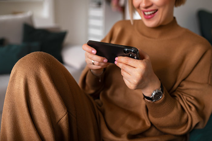Person in brown outfit smiling while using smartphone, enjoying daily dose of fascinating knowledge facts.
