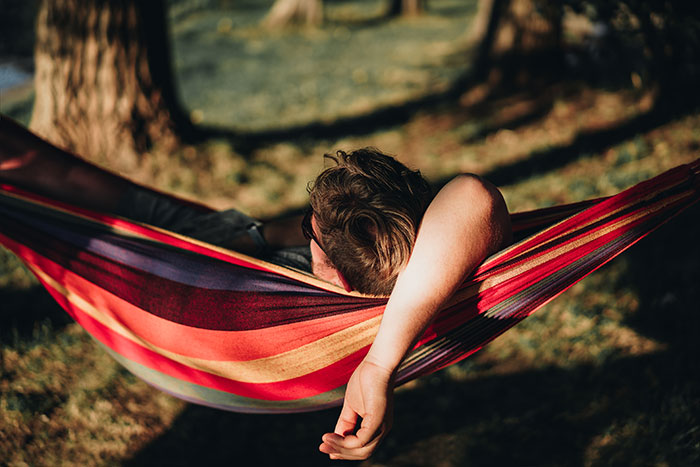 Person relaxing in a colorful striped hammock outdoors, enjoying a peaceful moment of daily dose of fascinating knowledge.
