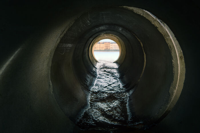 View inside a sewer pipe showing flowing water and light at the end, related to sewer workers' bizarre discoveries.