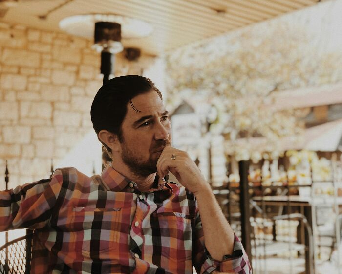 Man in a checkered shirt sitting in a cafe, appearing deep in thought, representing crazy stories servers overheard.