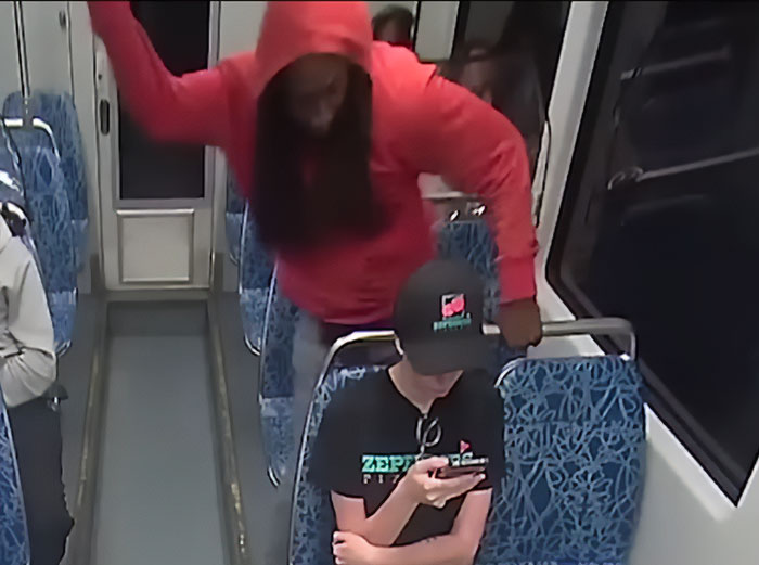 Person in red hoodie standing behind seated person wearing a cap on public transit, related to Iryna Zarutska brutal crime case.