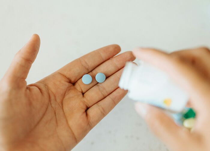 Hand holding two blue pills with a medicine bottle pouring more, symbolizing treatment for meningitis risk in a young girl.
