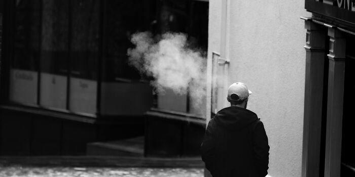 Man wearing cap exhaling smoke while standing alone near building, symbolizing the fastest ways someone got fired.