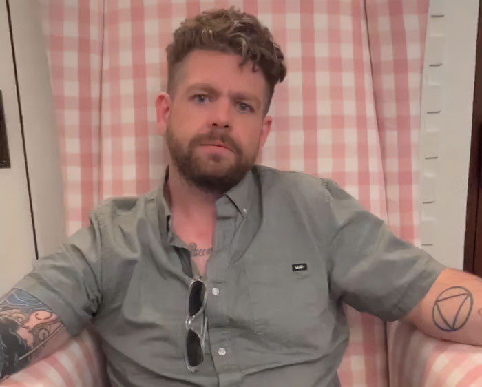 Man with tattoos and beard sitting in a chair, related to Roger Waters and Ozzy Osbourne son responding to criticism. Man with tattoos and beard sitting in a chair, related to Roger Waters and Ozzy Osbourne son responding to criticism.