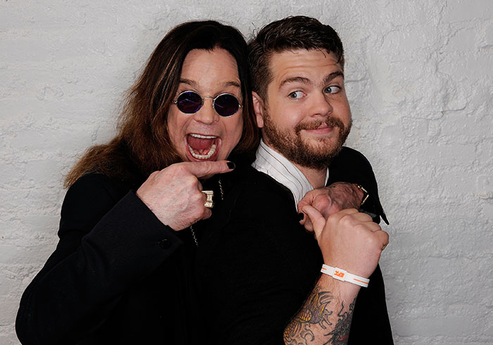 Ozzy Osbourne and his son posing playfully against a white brick wall, highlighting family and music legacy. Ozzy Osbourne and his son posing playfully against a white brick wall, highlighting family and music legacy.